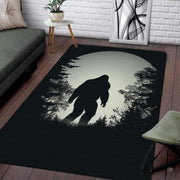 Bigfoot Sasquatch silhouette walking beneath silver full moon in forest rectangular area rug. - thumbnail image 1 of 5