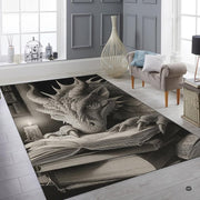 Charcoal fantasy dragon resting its head and claws on an open spellbook beside a candle in an ancient library area rug. - thumbnail image 6 of 8